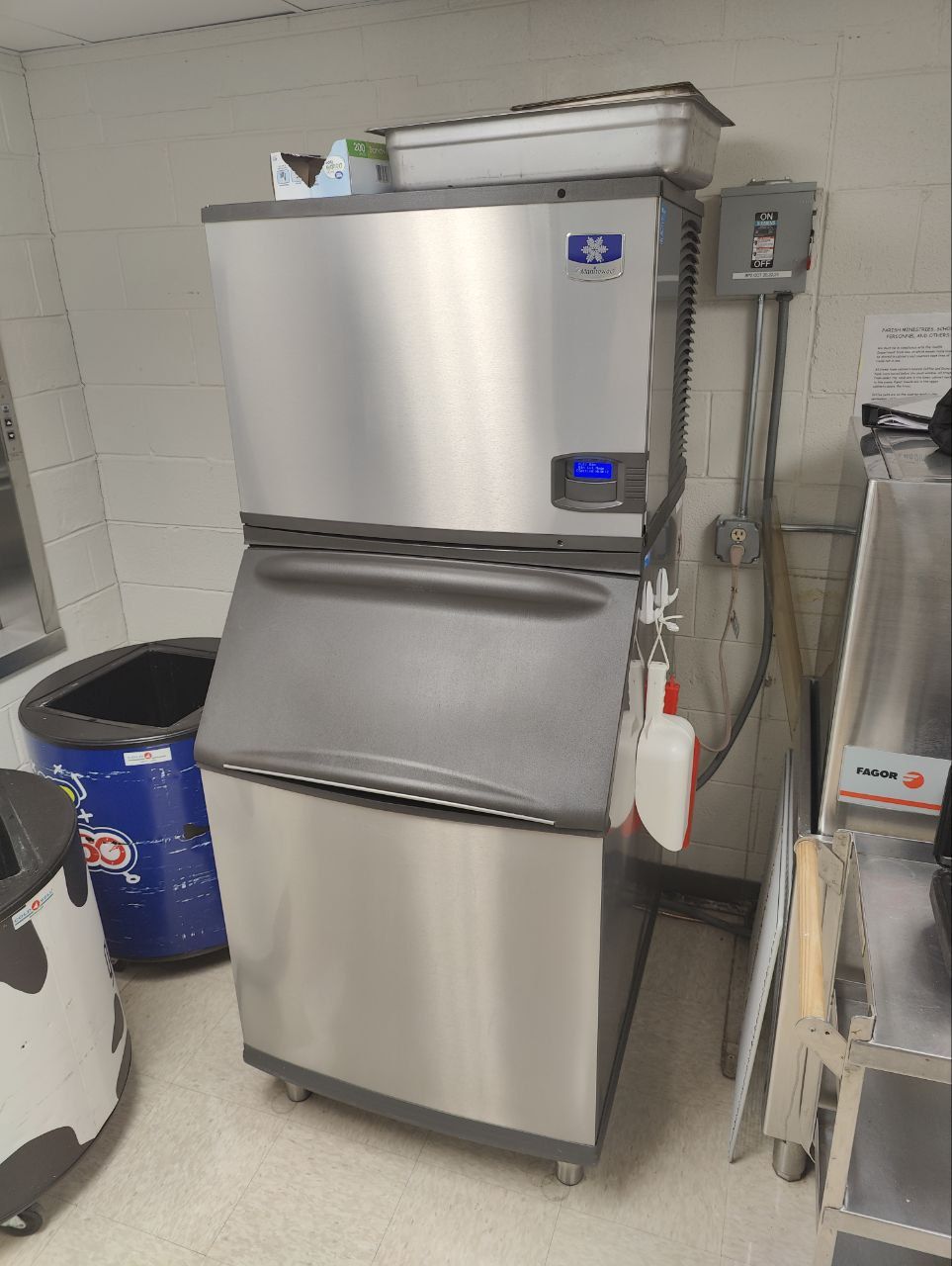 Stainless steel ice machine above a storage bin in a utility space