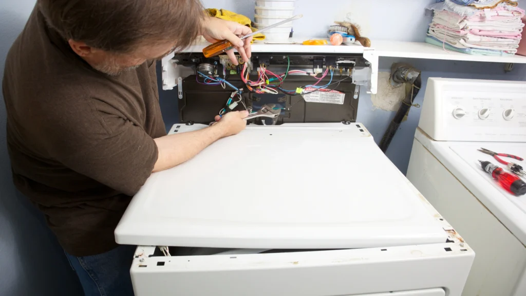Person examining wiring behind an opened dryer control panel