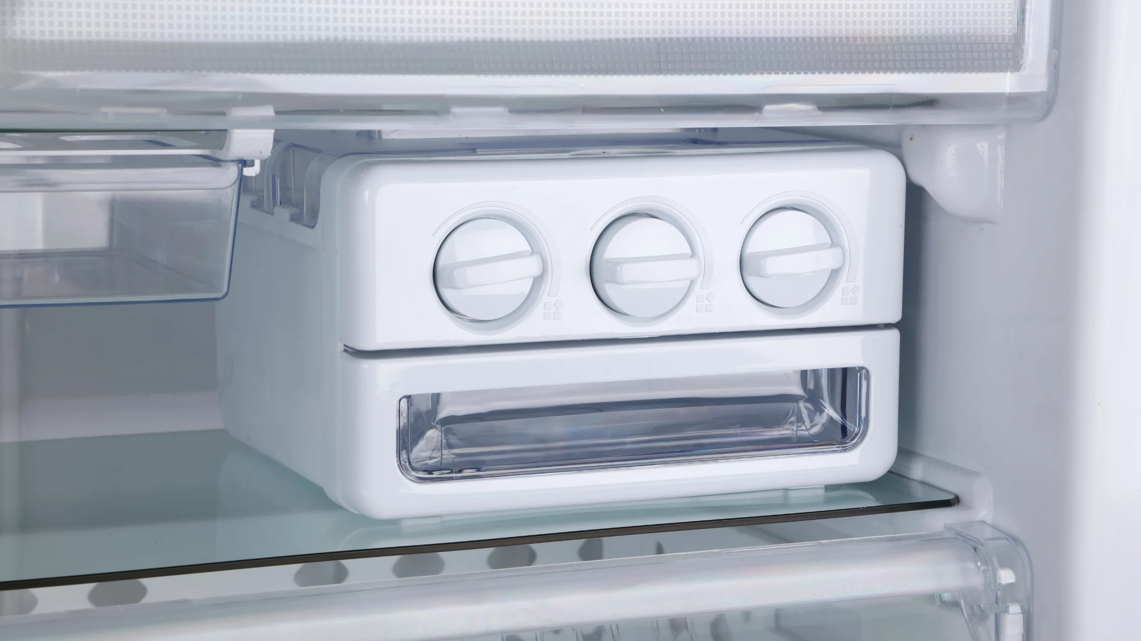 Three manual ice-tray knobs above a clear storage bin inside a freezer