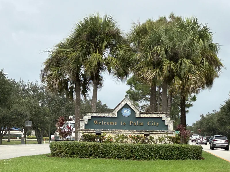 Welcome to Palm City sign among palms beside a road